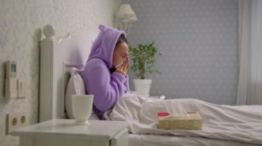 Hasta 20 'li yaşlardaki Asyalı kadın öksürüyor ve evde yatağında peçetelerle burnunu siliyor. Grip ve diğer solunum hastalıkları.