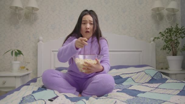 Millennial Asian soccer fan watching game with popcorn. Woman celebrates victory goal of favourite team in front of tv looking at camera sitting in bedroom. — Video Stock