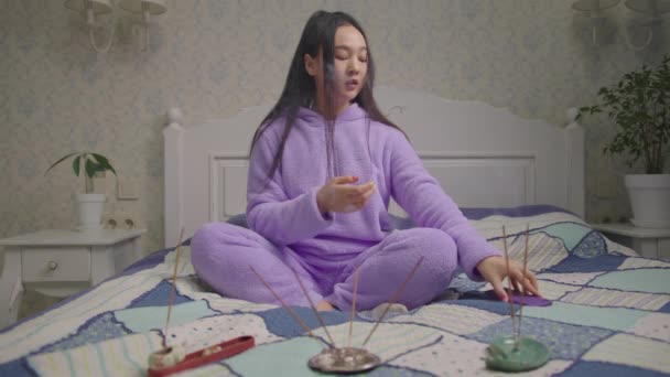 Ázsiai nő mobiltelefont használ meditációs gyakorlatra, otthon ül az ágyon. Nő légzési gyakorlatot végez közvetítő alkalmazással mobiltelefonon. — Stock videók