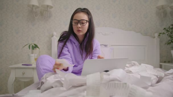 Сконцентрована азіатка в окулярах, дивиться на скарбниці, що сидять у ліжку. 20-ті жіночі рахунки сімейний бюджет за допомогою ноутбука. — стокове відео