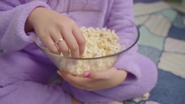 Asyalı bir kadının film ya da televizyon izlerken patlamış mısır yemesine yakın çekim. Mor pijamalı kadın patlamış mısır yiyor. El kamerası..