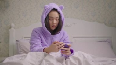 Milenyum Asyalı kadın cep telefonuyla oyun oynuyor ve yatakta oturarak oyunu kazanıyor. Kadın cep telefonuyla oynarken evet diyor. Kazandığıma sevindim..