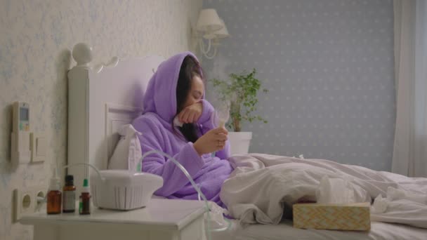 Young 20s ill Asian woman using inhaler for therapy of disease like flu or respiratory viruses at home. Female treating cough with medicine inhaler machine lying in bed. — Stock Video