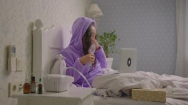 Genç, hasta, Asyalı bir kadın, elinde astım spreyi olan bir doktorla görüntülü konuşma yapıyor. Kadın öksürüğü ilaç solunum cihazıyla tedavi ediyor. Evde grip ya da solunum virüsü tedavisi.