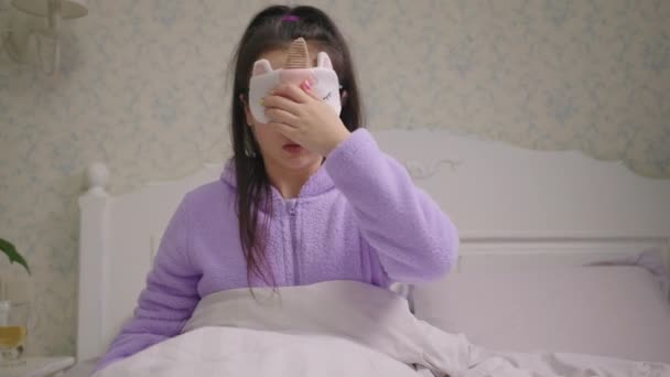 20s femme asiatique se réveiller dans le masque de sommeil et en regardant le téléphone mobile se rendant compte qu'elle est en retard. Femme en pyjama violet surdort. — Video