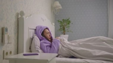 20 'li yaşlardaki Asyalı kadın yatakta öksürüyor. Evde kalan hasta bir kadın..