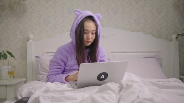 Exited 20s Asian woman reads good news on laptop sitting in bed. Young adult woman is very happy kissing laptop. Cheerful woman shows wow emotion. — Wideo stockowe