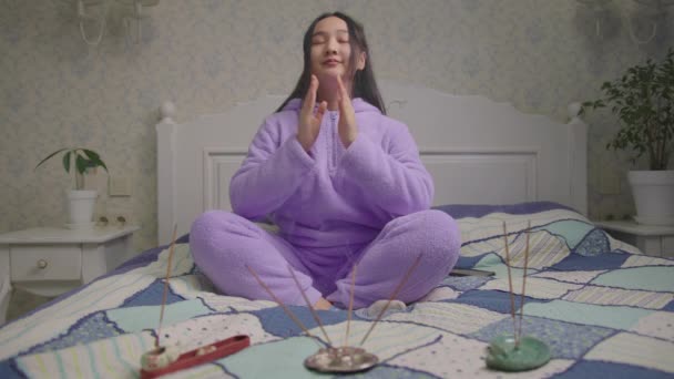 20s Asian woman doing breathing exercise and meditation practice at home. Female resting sitting on bed with aroma sticks. Easy to meditate at home. — Stockvideo