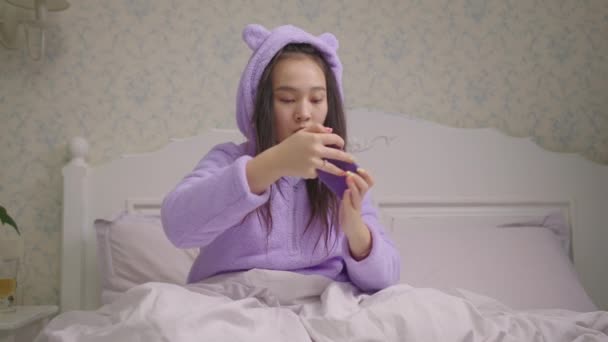 Aziatische vrouw uit de 20 die videospelletjes speelt op de mobiele telefoon en het spel op bed wint. Lady maken triomf gebaar tijdens het spelen op de smartphone. Blij om te winnen. — Stockvideo