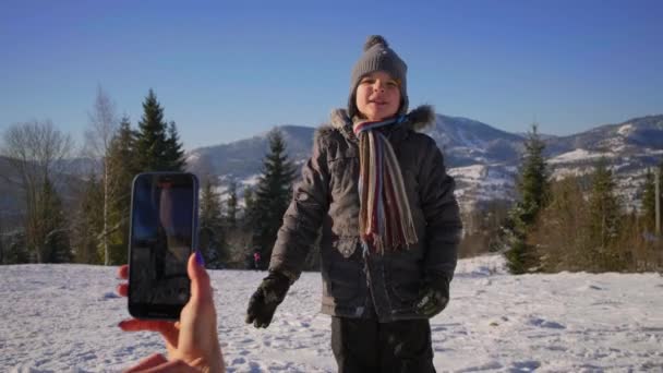 Matki nagrywają wideo na komórce syna tańczącego na zimowej górze. Rodzinne filmy wideo dla mediów społecznościowych dzieci taniec na zewnątrz. — Wideo stockowe