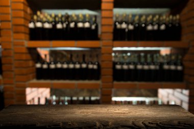 Arkaplanda şarap şişeleri ve bir bardak light bira olan boş ahşap masa.