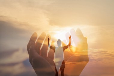 Başarı ve maneviyat özgürlüğü kavramı. Güneşli bir günbatımının arka planında ellerini kaldırarak dua eden bir kadın..