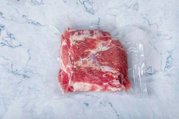 The meat in a vacuum bag lies on the background of marble.