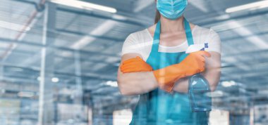 Bir temizlikçi kadın bulanık endüstriyel arka planda pencerenin önünde duruyor..