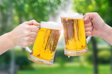 Birayla yaz tatili. Bardaklar dolusu bira parkın arka planına çarpıyor..