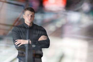 Young businessman standing with his arms crossed against a blurred background.