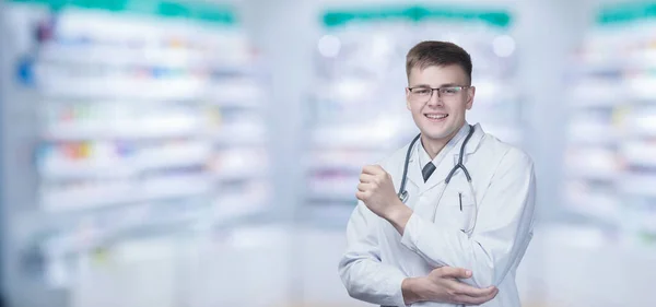 Young medical specialist smiling on blurred pharmacy background.