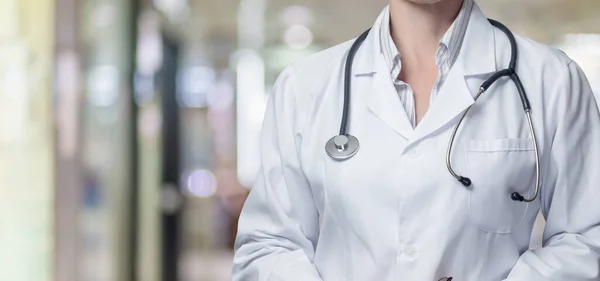 A doctor stands on a blurred background of a hospital or clinic.