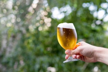 Hand with a glass of beer in the blurred background.