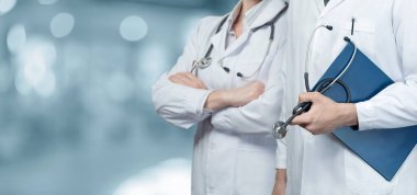A group of medical workers stand in front of a blurred background of a hospital.
