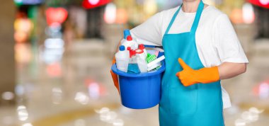 Concept of a well done cleaning. Cleaning lady shows hand ok on blurred background.