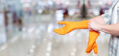 A cleaning lady puts a rubber glove on her hand on a blurred background of a store.
