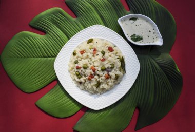 Hintli irmikli kahvaltı, beyaz tabakta servis edilen sağlıklı yemek. Sebze görünümünün üst görüntüsü Kırmızı ve yaprak arkaplan, yazı tipi metni yazmak için boşluk. Hint yemeklerinin üst görünümü