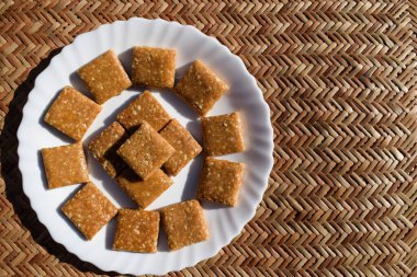 Tatlı, tatlı, ezilmiş fıstıklı chikki beyaz tabakta fotokopi alanı boş. Yazı tipleri için tebrik dilekleri yazmak için. Mutlu makar sankrant posterleri ahşap hasır arka planda