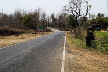 Madhya Pradesh 'teki ormandaki Ghat Dağı' ndaki karayolunda yolun her iki tarafında beyaz çizgiler ve kurumuş ağaçlar var. Yaz günü Dhaba Motel 'in yanındaki lastik dükkanında.