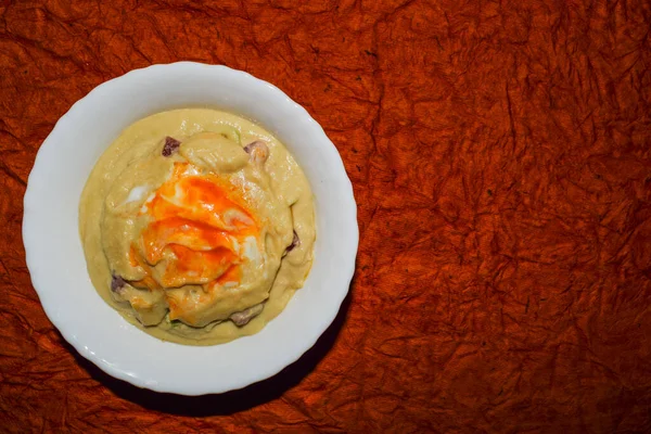 Turkish or Arabic food cuisine Hummus or Humus served in bowl. Hummud dip garnished with red chilly paprika and olive oil served in white bowl with dark orange tectured background top view