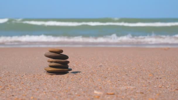 Fala morska toczy się na piaszczystym brzegu. Kupa kamieni jest ułożona w piramidzie. Medytacja zen, harmonia, równowaga — Wideo stockowe