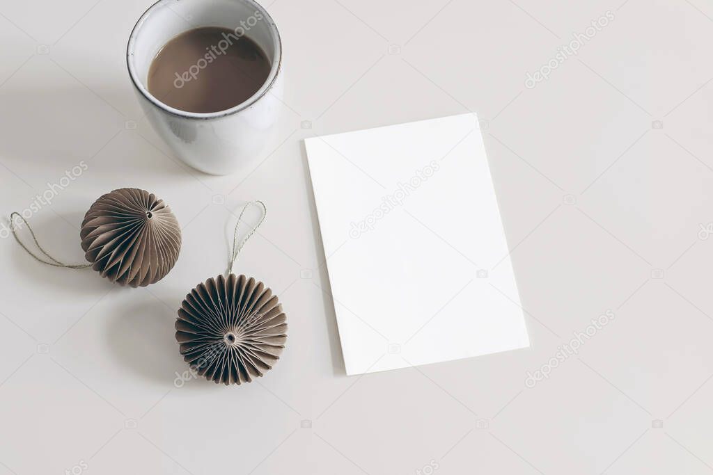 Winter holiday stationery mockup. Brown paper Christmas ornaments and cup of coffee isolated on white table background. Blank greeting card, invitation, flat lay, top view. No people. Paper balls.