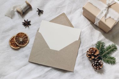 Noel hediyesi paketleme natürmort. Spruce ağacı dalları, hediye kutusu ve kuru portakal dilimleri. Boş kart modeli, el işi zarf ve çam kozalakları. Beyaz keten masa örtüsü arka planı. Flatlay, üst görünüm.