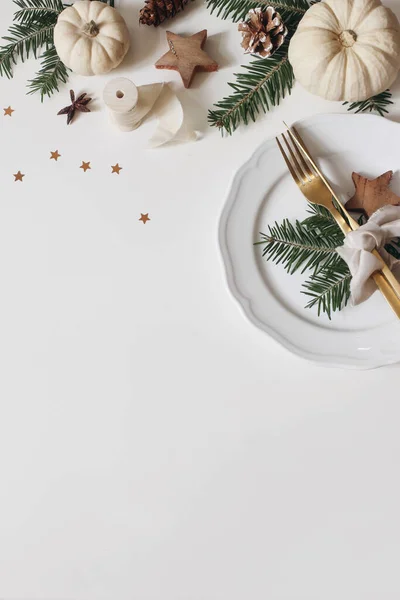 Cenário festivo da mesa de Natal. Talheres dourados, ramos de abeto. Abóboras brancas isoladas em fundo branco. cones de pinheiro, decoração de estrelas de confete. Composição de inverno. Colocação plana, vista superior, vertical — Fotografia de Stock