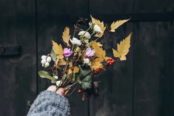 Photo de stock stylisée. Composition féminine d'automne. Gros plan de mains de femmes tenant des fleurs et des feuilles d'automne colorées bouquet. Cyclamen rose et baies rouges. Fond de porte vintage flou foncé. — Photo