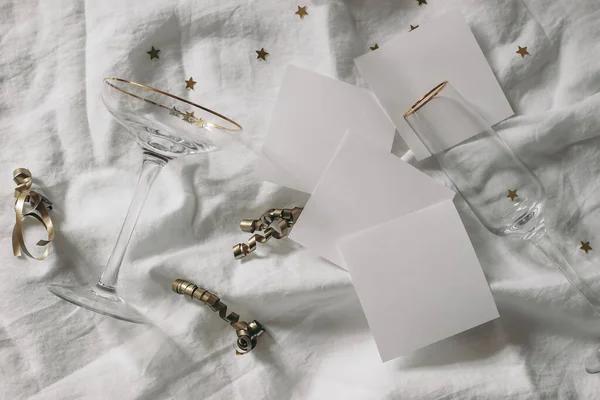 Happy New Year composition. Blank note pads mockups scene. Champagne glasses with golden confetti stars. White wrinkled linen table cloth background. Celebration, party concept. Flat lay, top view. — Stockfoto