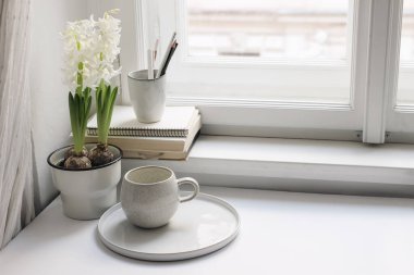 Bahar hala hayattır. Kitaplar ve boş günlükler pencere pervazında. Çiçek saksısında beyaz sümbül. Bir fincan kahve. Seramik tutacakta kalemler. Merkez ofis konsepti. İskandinav iç mimarisi. Paskalya konsepti.