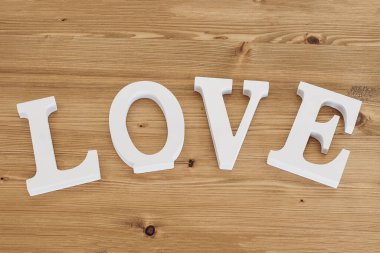 White word Love. Decorative text, letters. Wooden background. Festive banner. Happy Valentines Day, Mothers Day, March 8, World Womens Day holiday card concept. Wedding decor. Flat lay, top view.
