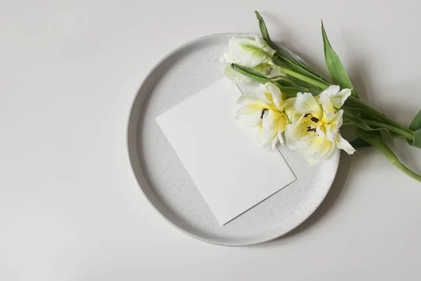 Easter holiday styled stock photo. Spring desktop mockup scene, banner. Green parrot tulip flowers. Blank greeting, card mockup on ceramic plate isolated on white table background. Flat lay, top view. — Stock Photo, Image