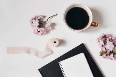 Paskalya, bahar hala hayat. Boş günlük maketi. Bir fincan kahve, çiçek açan pembe Japon kiraz ağacı dalları beyaz masa arkasında izole edilmiş. Merkez ofis. Kahvaltı, kavramı bozmak. Düz yatış, üst görünüm.