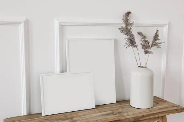 Set von weißen Bilderrahmen-Attrappen. Vase mit trockenem Schilf, Gras auf alter Holzbank. Wandleiste Hintergrund, Verkleidung Dekor. Elegante Inneneinrichtung Stillleben Foto. Kunst zum Anfassen. Seitenansicht. — Stockfoto