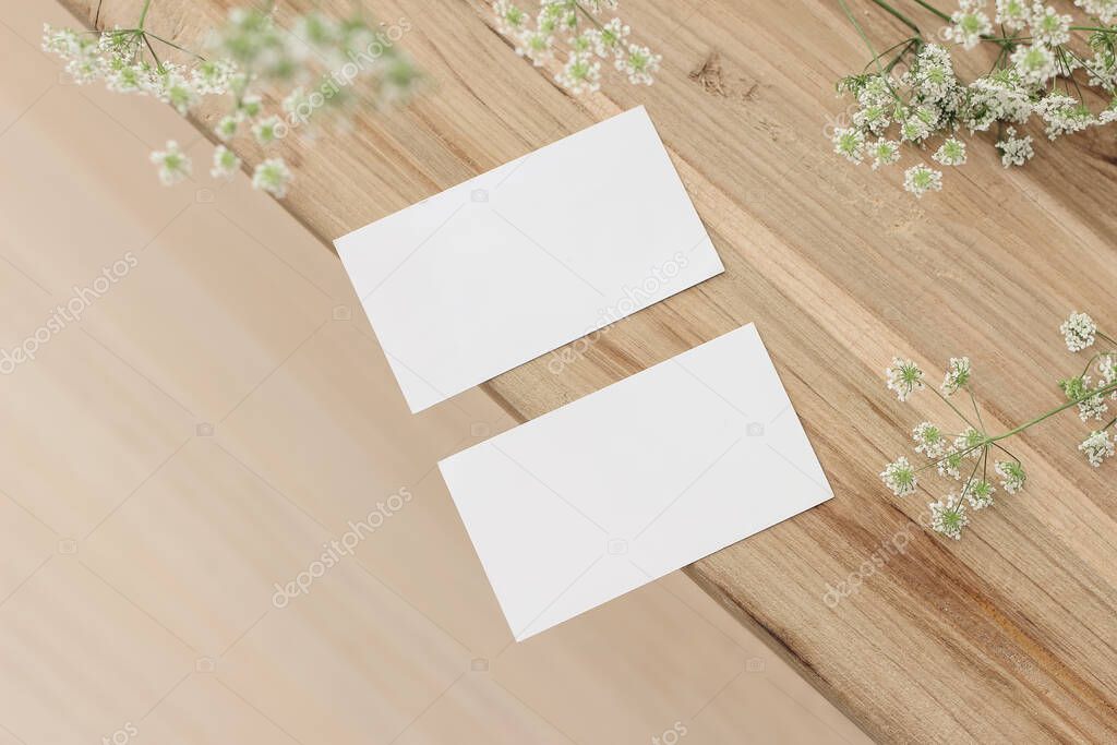 Set of two blank business cards and cow parsley flowers. Old wooden table. Flat lay, top view, selective focus, blurred background. Feminine stationery. Wedding, birthday desktop mock-up scene.