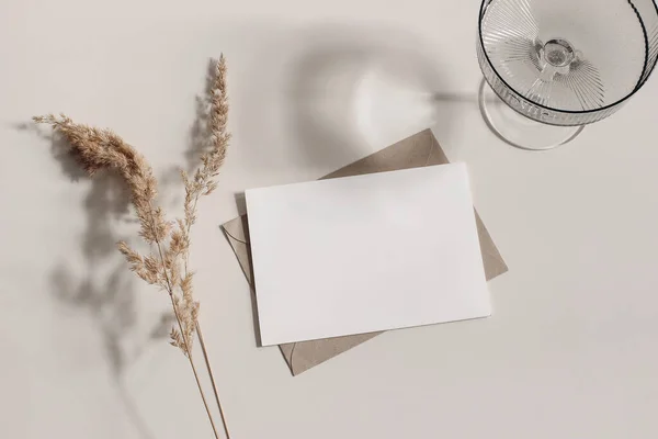 Feminine stationery still life. Champagne, cocktail glass, shadows. Blank greeting card, invitation mockup, craft envelope. Dry grass, festuca plant in sunlight. Beige table background. Fall flatlay — Stock Photo, Image