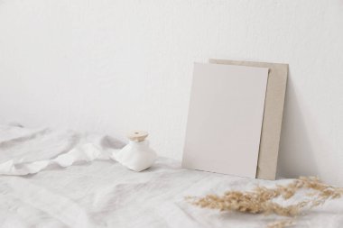 Düğün kırtasiyesi hala hayat dolu. Boş pembe tebrik kartı, davetiye maketi, ipek kurdele ve çarşaf masa örtüsüne yapıştırılmış el işi zarf. Beyaz duvar. Bulanık kuru otlar festuca