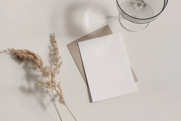 Feminine fall stationery still life. Cocktail grey glass, long shadows. Blank vertical greeting card, invitation mockup, craft envelope, flatlay. Dry grass festuca, sunlight. Beige table background. — Stock Photo, Image