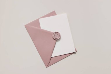 Boş düğün kartı, gün ışığında davetiye çıkartma sahnesi. Üzerinde dekoratif balmumu mühür olan pembe zarfın yakın çekimi. Doğum günü kırtasiyesi şablonu. Düz yerde, üst tarafta. Kadınsal bileşim.