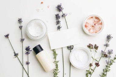 Kartvizit modeli. Cilt kremi, nemlendirici ve şampuan şişesi. Lavanta, kekik otu ve Himalaya tuzlu satürja otları. Beyaz masa arka planı, organik kozmetik ürünleri, spa konsepti. Düz yatış, üst görünüm.