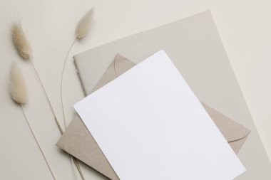 Boş kağıt tebrik kartı, davetiye ve günlük modelinin kapanışı. Boho kırtasiyesi hala hayat dolu. Lagurus yumurtası, tavşan kuyruğu çimenli bitki örtüsü. El işi zarfı. Bej tablo arkaplanı, nötr üst görünüm.