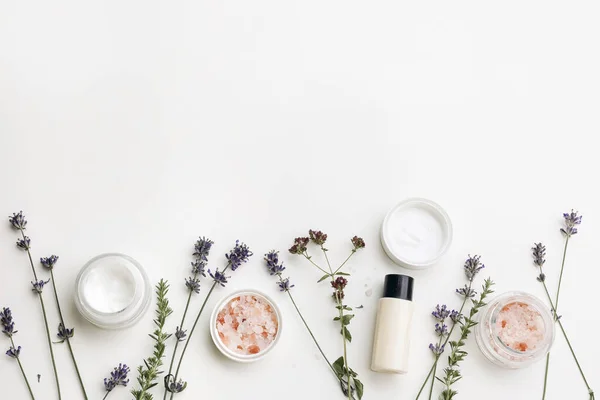 Organic beauty cosmetics frame, web banner. Skin cream, moisturizer and shampoo bottle isolated on white table background. Lavender, oregano and satureja herbs, Himalayan salt. Spa concept. Flat lay.
