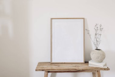 Winter, fall still life. Dry grass, plant bouquet in rustic ceramic vase. Old books on wooden bench. Blank vertical picture frame mockup. White wall background, empty copy space. Scandinavian nterior